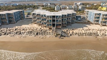 A beachfront hotel with multiple balconies, a sandy beach in front, and a view of the ocean.