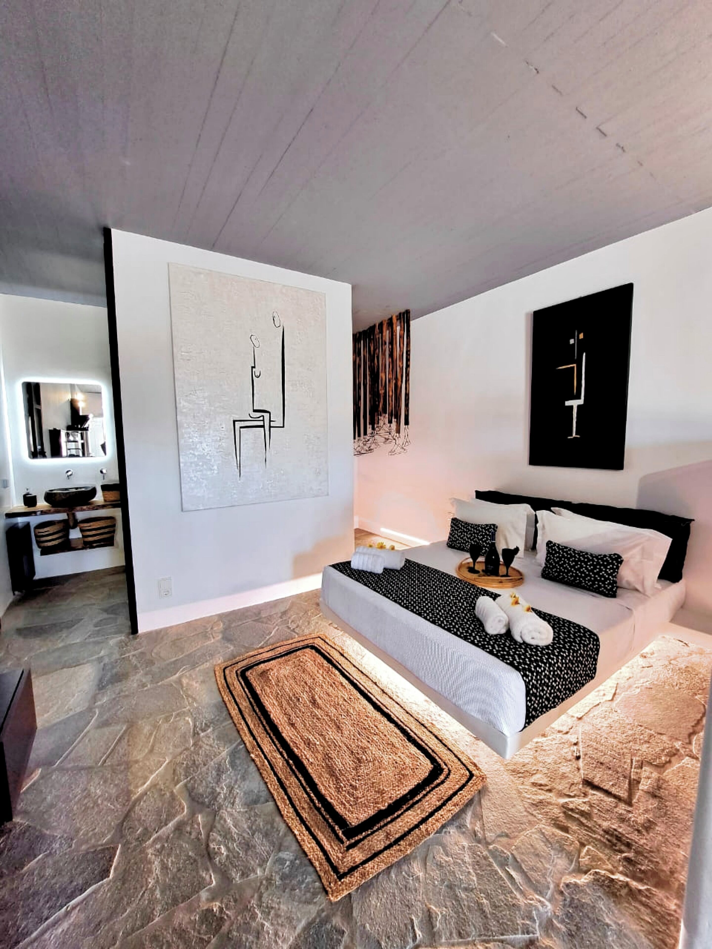 A modern bedroom with a large bed, a small bedside table, a mirror, and abstract wall art.