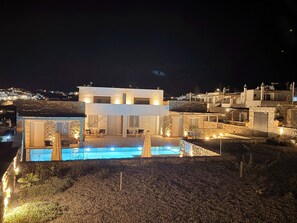 Eine moderne Villa mit Pool, Steinmauern und Blick auf die umliegende Landschaft bei Nacht.