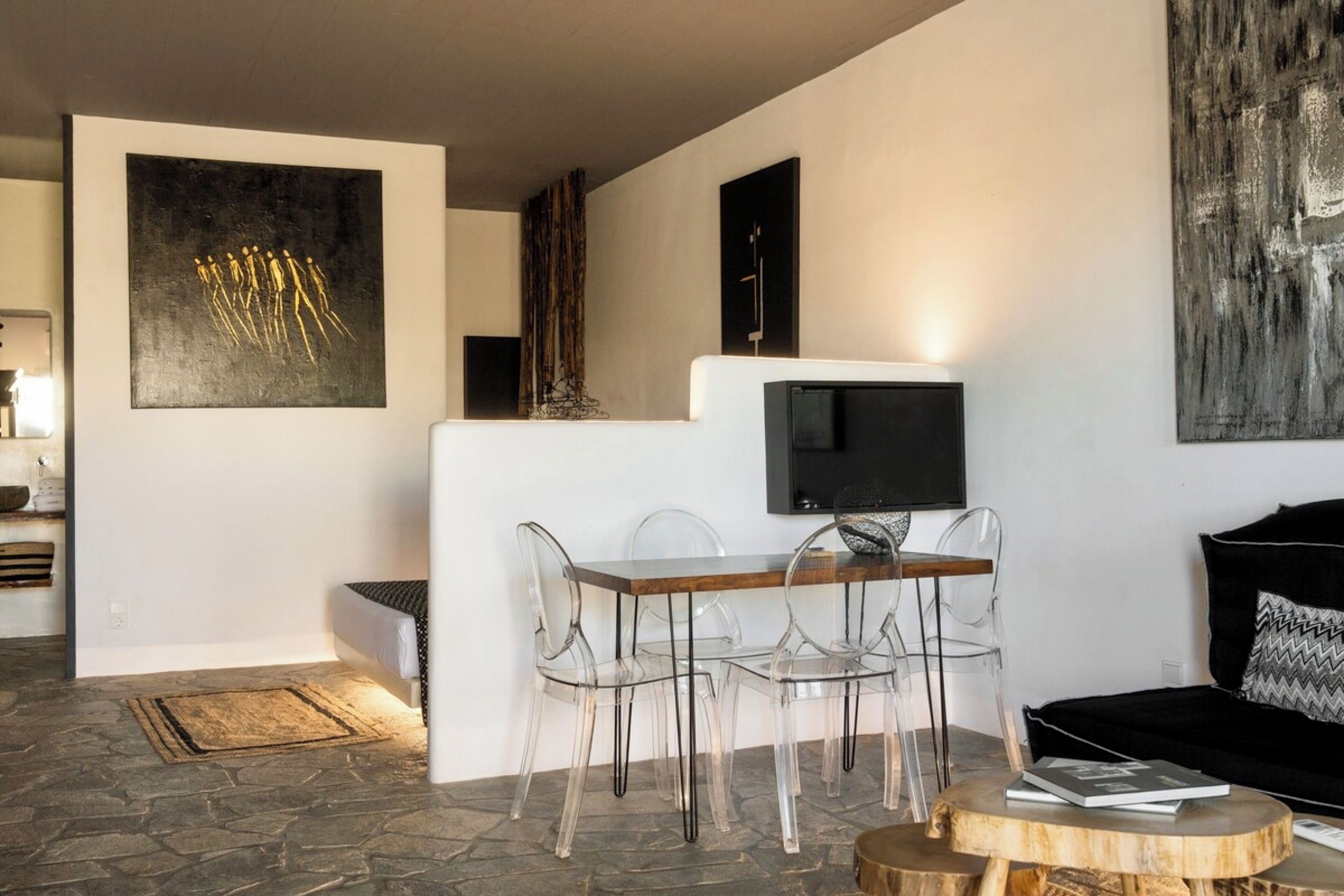 A modern living room with a stone floor, a dining area with clear chairs, a black sofa, and abstract art on the walls.