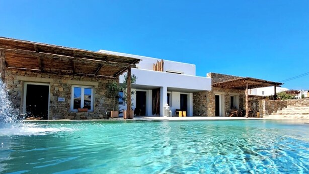 Un edificio moderno con fachada de piedra, piscina y cielo azul despejado.