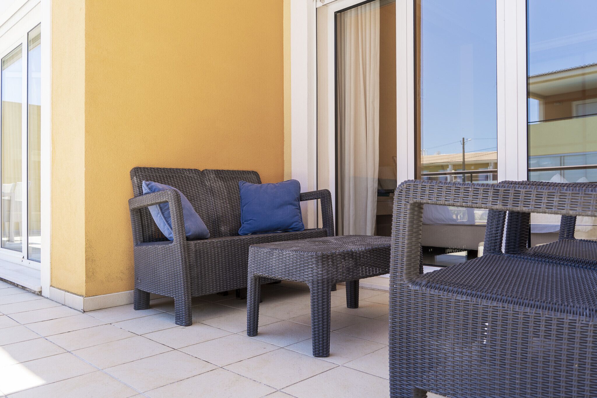 A balcony with wicker furniture, including a sofa and a chair, and a sliding glass door.