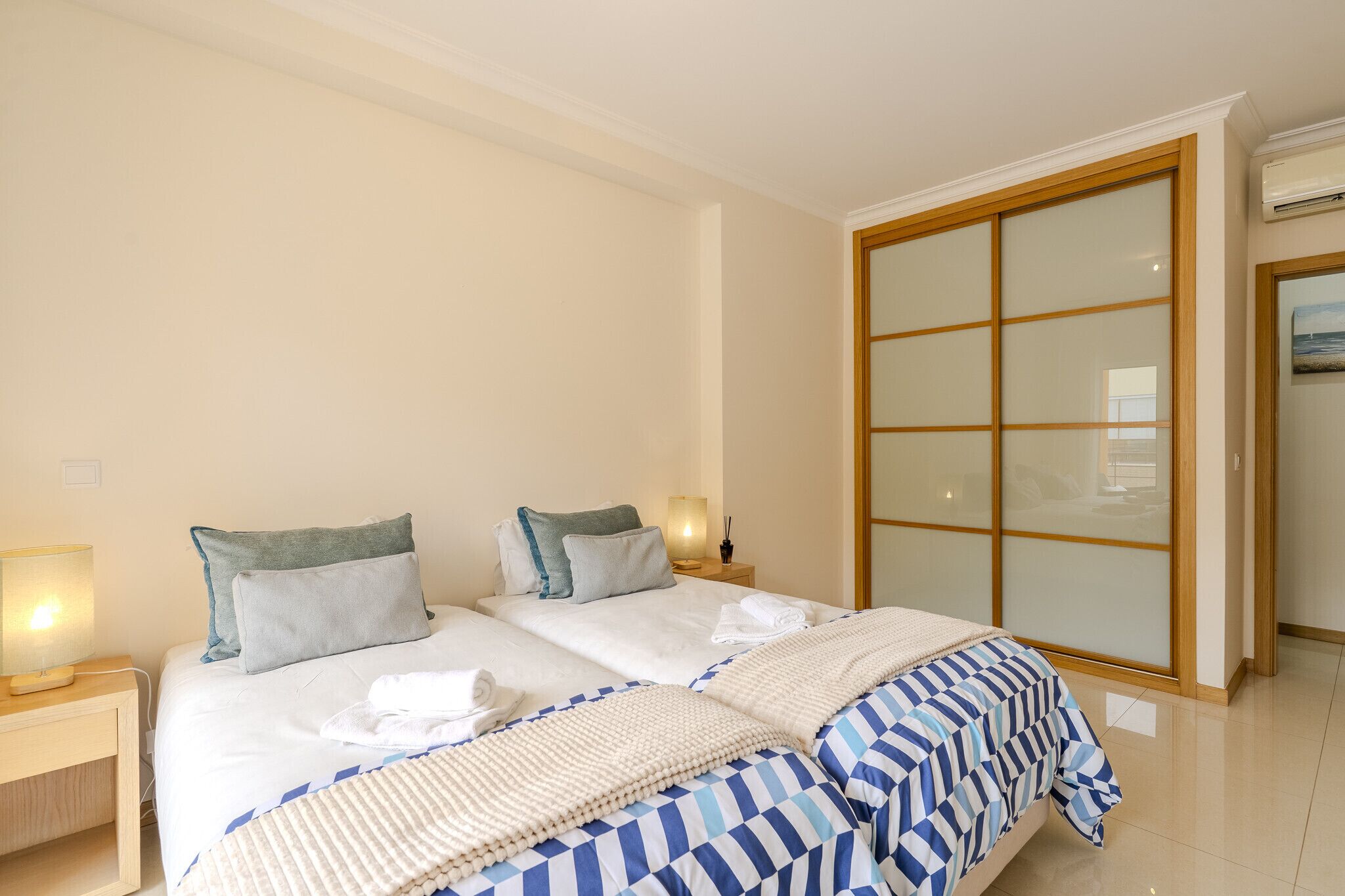 A double bed with a striped blanket, a bedside table with a lamp, and a sliding glass door.