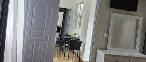 An open door leading to a dining area with a table and chairs, a dresser with drawers, and a mounted television.