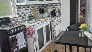 Een kleine keuken met witte kasten, een gasfornuis, een koffiezetapparaat en een eethoek met een tafel en stoelen.