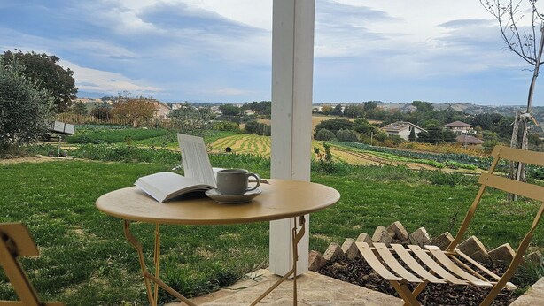 Uma área de estar coberta ao ar livre, com mesa e cadeiras, com vista para uma paisagem rural.