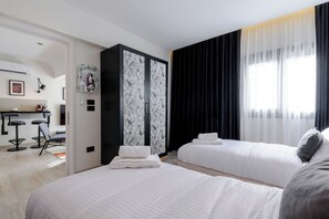 Ein Hotelzimmer mit zwei Betten, einem Kleiderschrank, einem Schreibtisch mit Stühlen und einem Fenster mit Vorhängen.