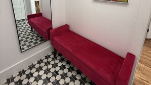 A hallway with a red bench, a large mirror, and two abstract paintings on the wall.