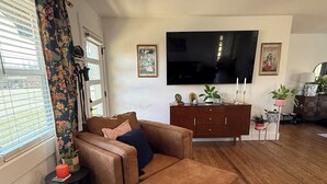A living room with a brown leather sofa, a television mounted on the wall, and a wooden floor.