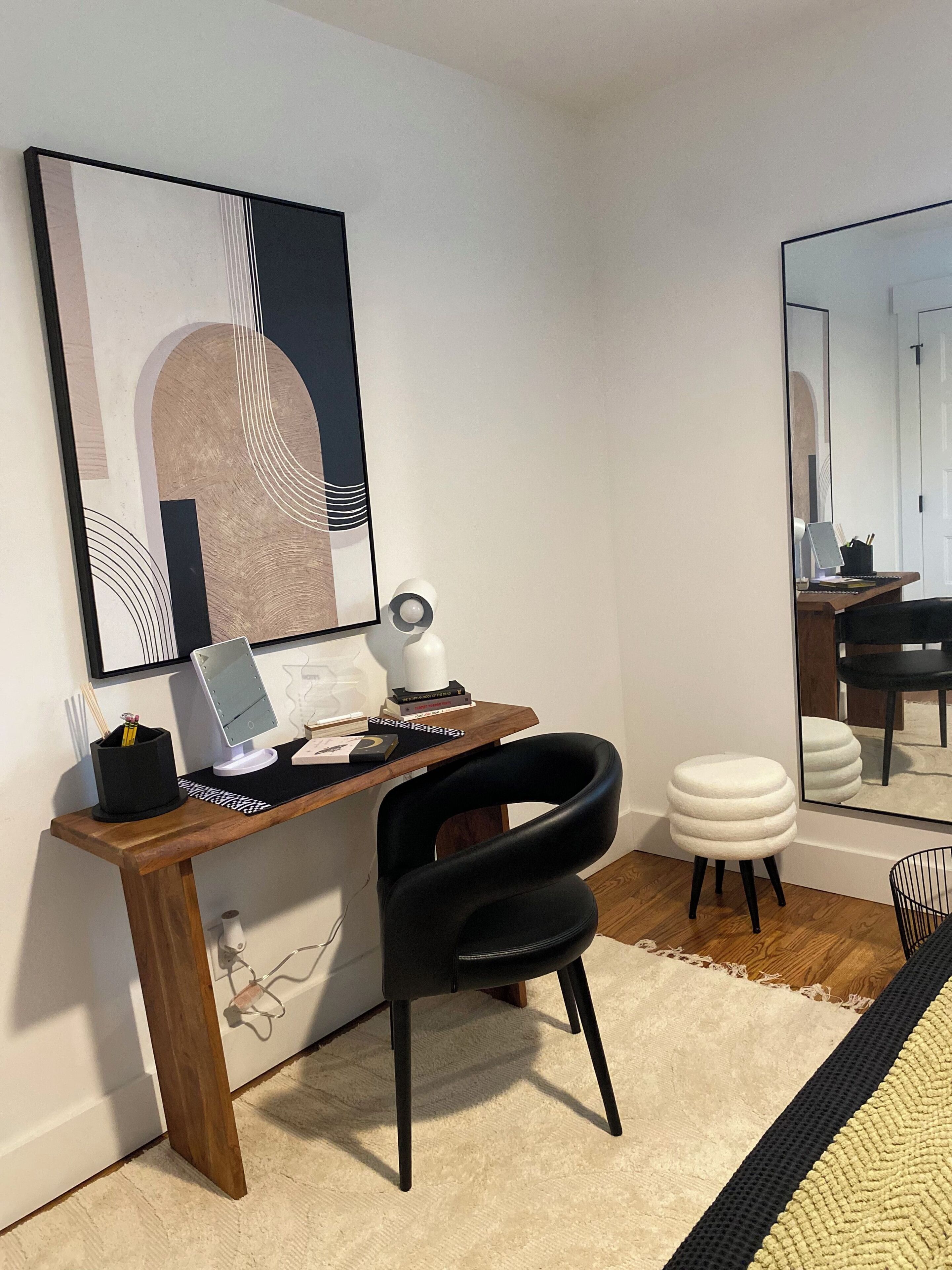 Un espace de bureau moderne avec un bureau en bois, une chaise noire, un tabouret blanc et un grand miroir.