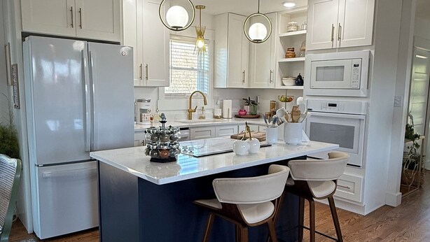 A modern kitchen with white cabinetry, a central island with bar stools, a refrigerator, and a microwave.