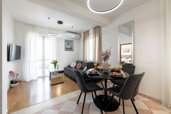 A modern living room with a sofa, dining table, chairs, and a TV. - Villa Nick-sunrise Deluxe Apartment (Konavle)
