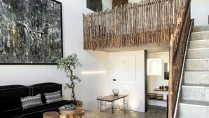 Uma sala de estar moderna com um sofá preto, uma mesa de centro de madeira, uma mesa de jantar transparente e uma escada com corrimão de madeira.