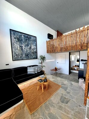 Ein modernes Wohnzimmer mit einer schwarzen Couch, einem großen abstrakten Gemälde, einer Holzwand und einem Steinboden.