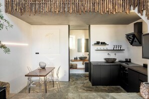 Una cocina moderna con piso de piedra, un comedor con sillas transparentes y una encimera negra con pileta.
