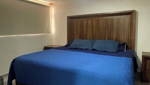 Un dormitorio con cama, cabecera de madera, mesitas de noche y una lámpara de techo.
