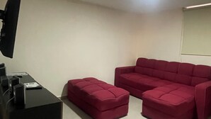Una sala de estar con un sofá modular, un televisor de pantalla plana y un mueble de entretenimiento negro.