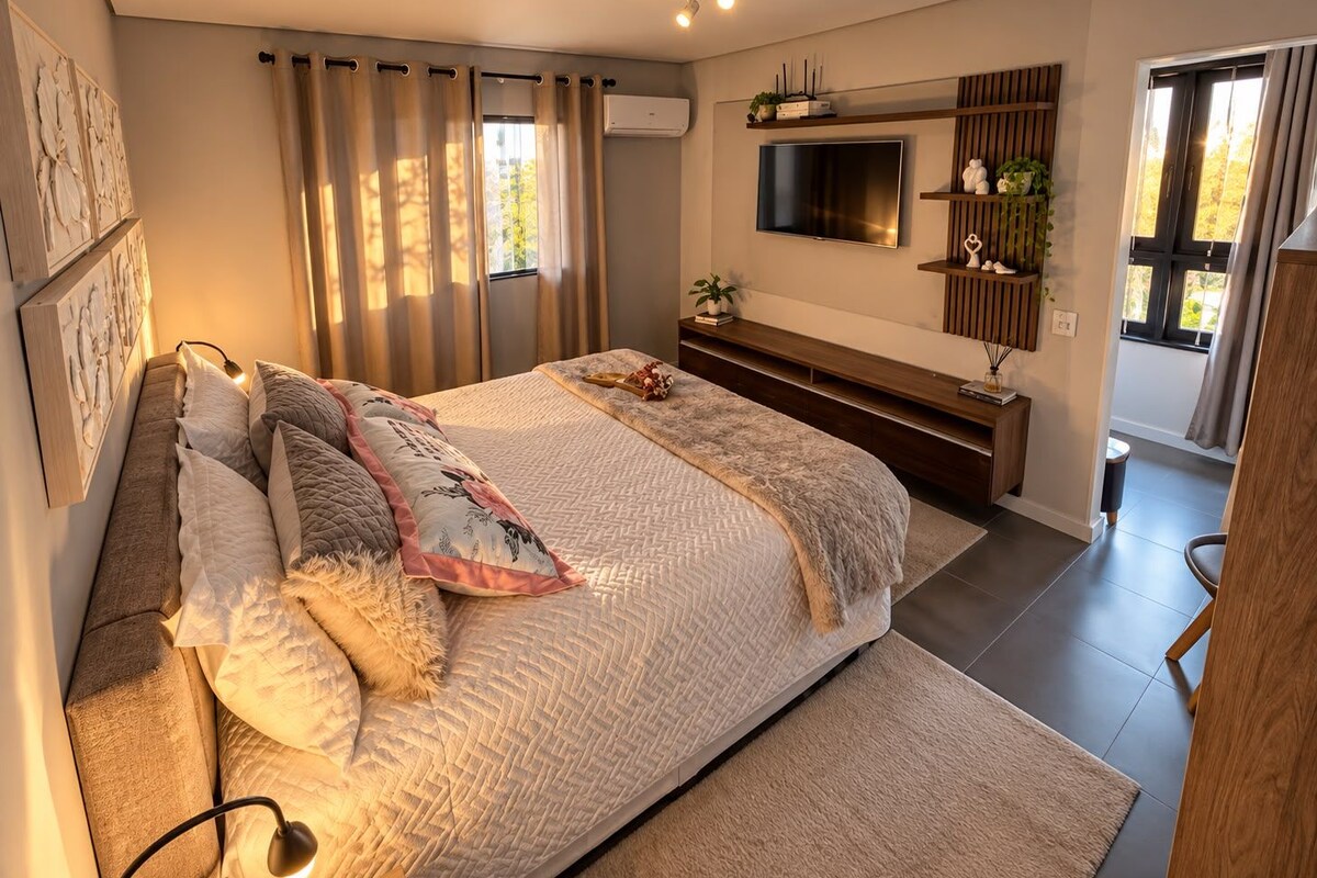 A modern bedroom with a large bed, a flat-screen TV, and a built-in bench.