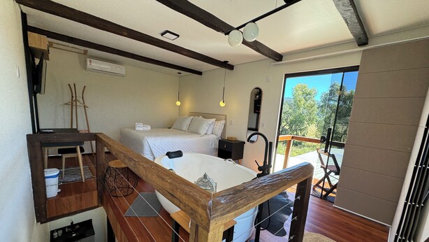A bedroom with a bed, bedside table, and a view of the outdoors.