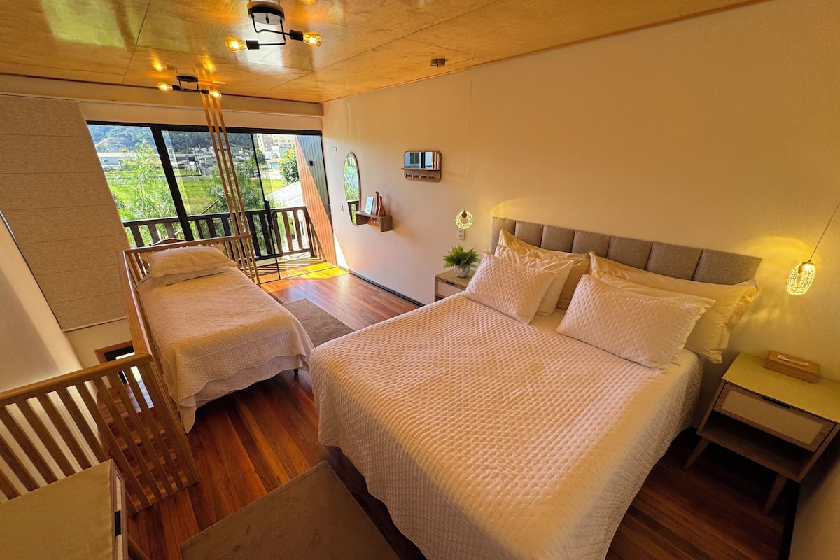 A bedroom with two beds, a balcony, a wooden floor, and a ceiling light fixture.