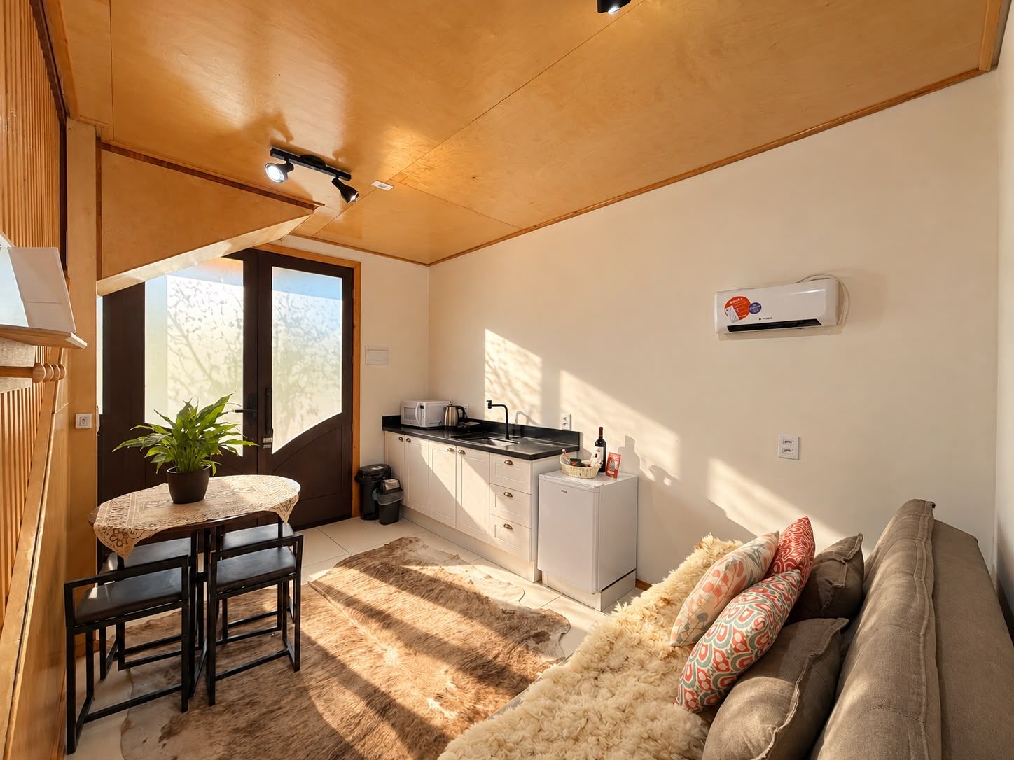 A compact living space with a dining area, kitchenette, and a sofa with decorative pillows.