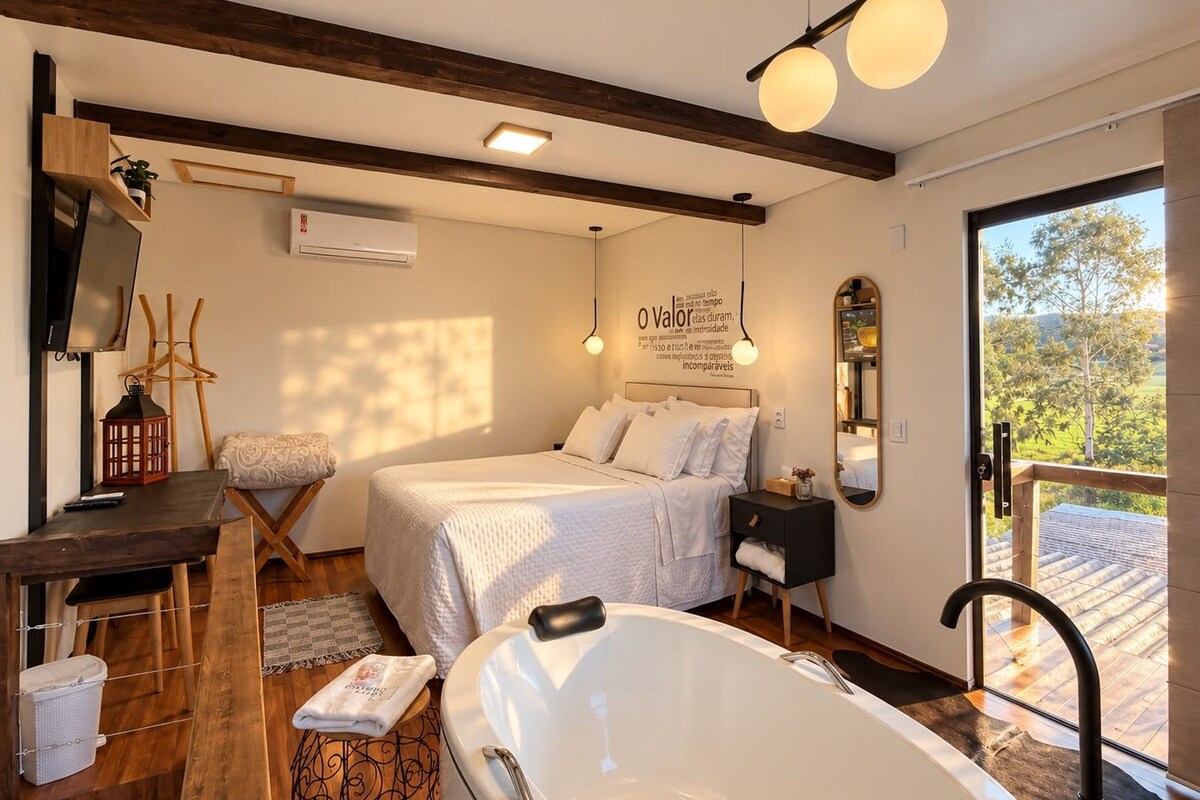 A bedroom with a bed, bedside table, lamp, and a view of the outdoors.