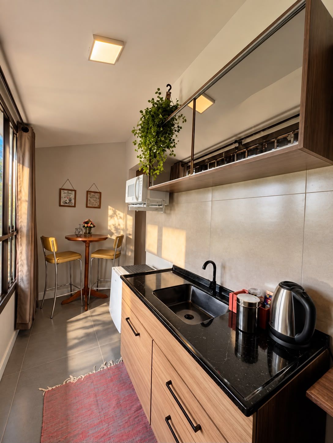 A compact kitchen with a black countertop, a stainless steel kettle, and a microwave. There is a small dining area with two chairs and a table.
