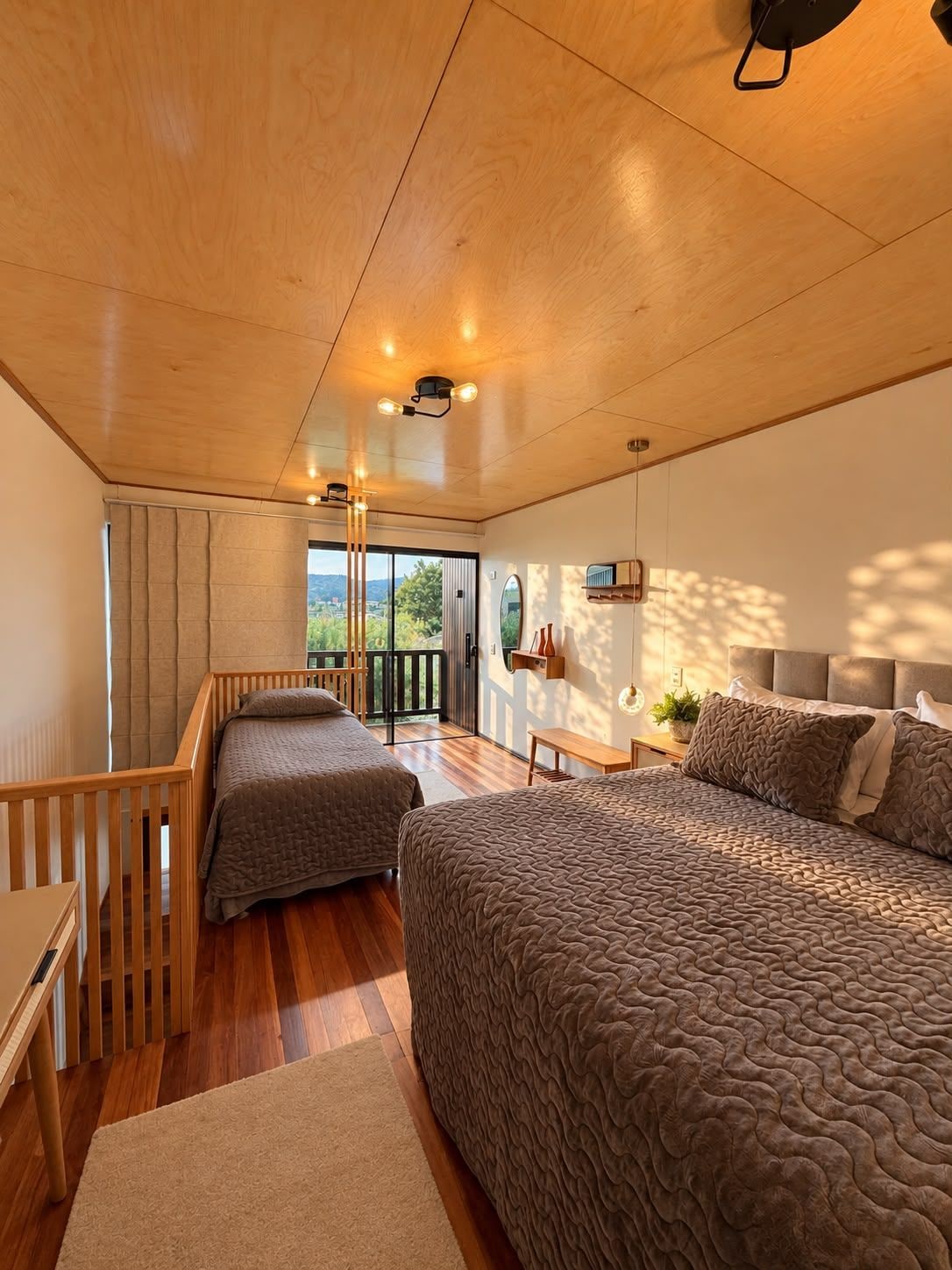 Un dormitorio con una cama grande, una cama más pequeña, techo de madera y vistas al exterior.