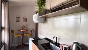A modern kitchen with a black countertop, stainless steel sink, and a kettle. There are wooden cabinets, a small table with chairs, and a potted plant.