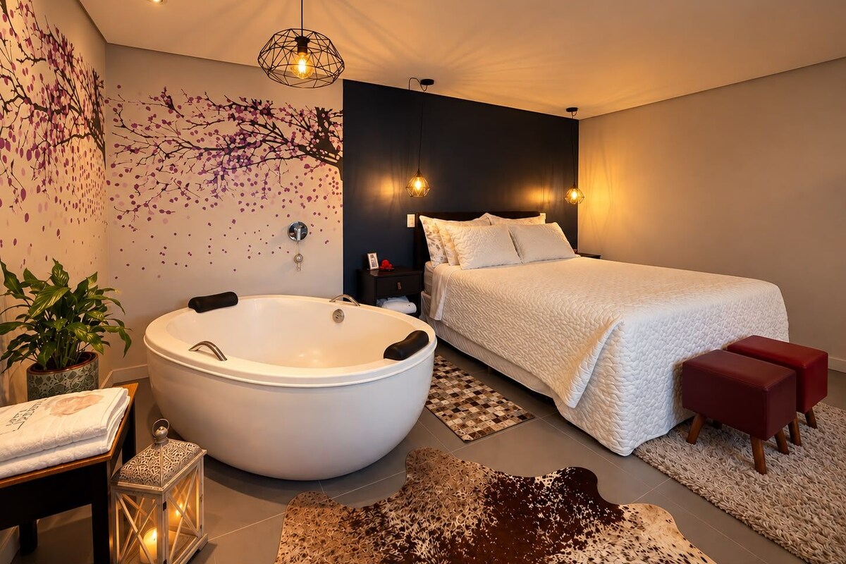 A modern bedroom with a large white bathtub, a bed with white bedding, and a dark accent wall.