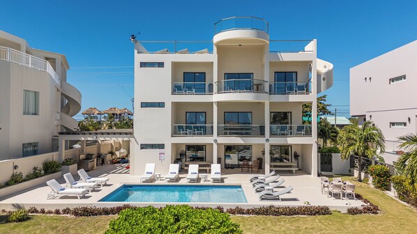 Un hotel de varios pisos con piscina, sillas de descanso y vistas al mar.