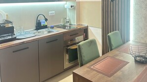Une cuisine moderne dotée d’appareils électroménagers intégrés, un coin repas avec une table et des chaises en bois, et un éclairage suspendu aux formes géométriques.