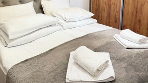 Un lit bien fait, avec du linge de lit blanc, une couvre-lit grise à motifs et une armoire en bois dotée de portes coulissantes.