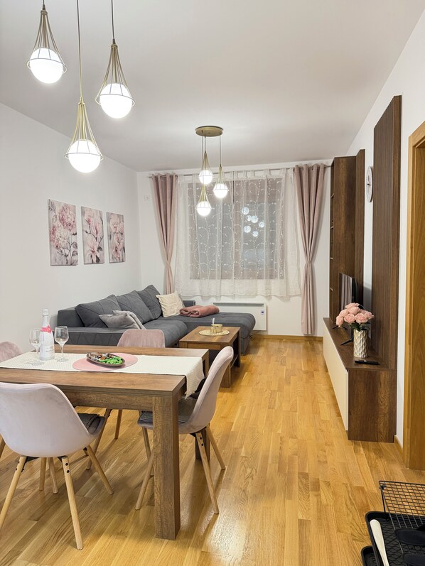 Una sala de estar moderna con comedor, suelo de madera y un televisor sobre un mueble de madera.