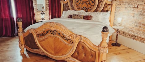 Een bed met een sierlijk houten hoofdeinde en voeteneinde, een spiegel en een lamp aan een bakstenen muur.