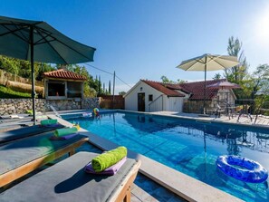 A swimming pool with lounge chairs and umbrellas, a stone wall, and a small building with a red roof. - Rustic Villa in Gruda With Private Pool (Konavle)