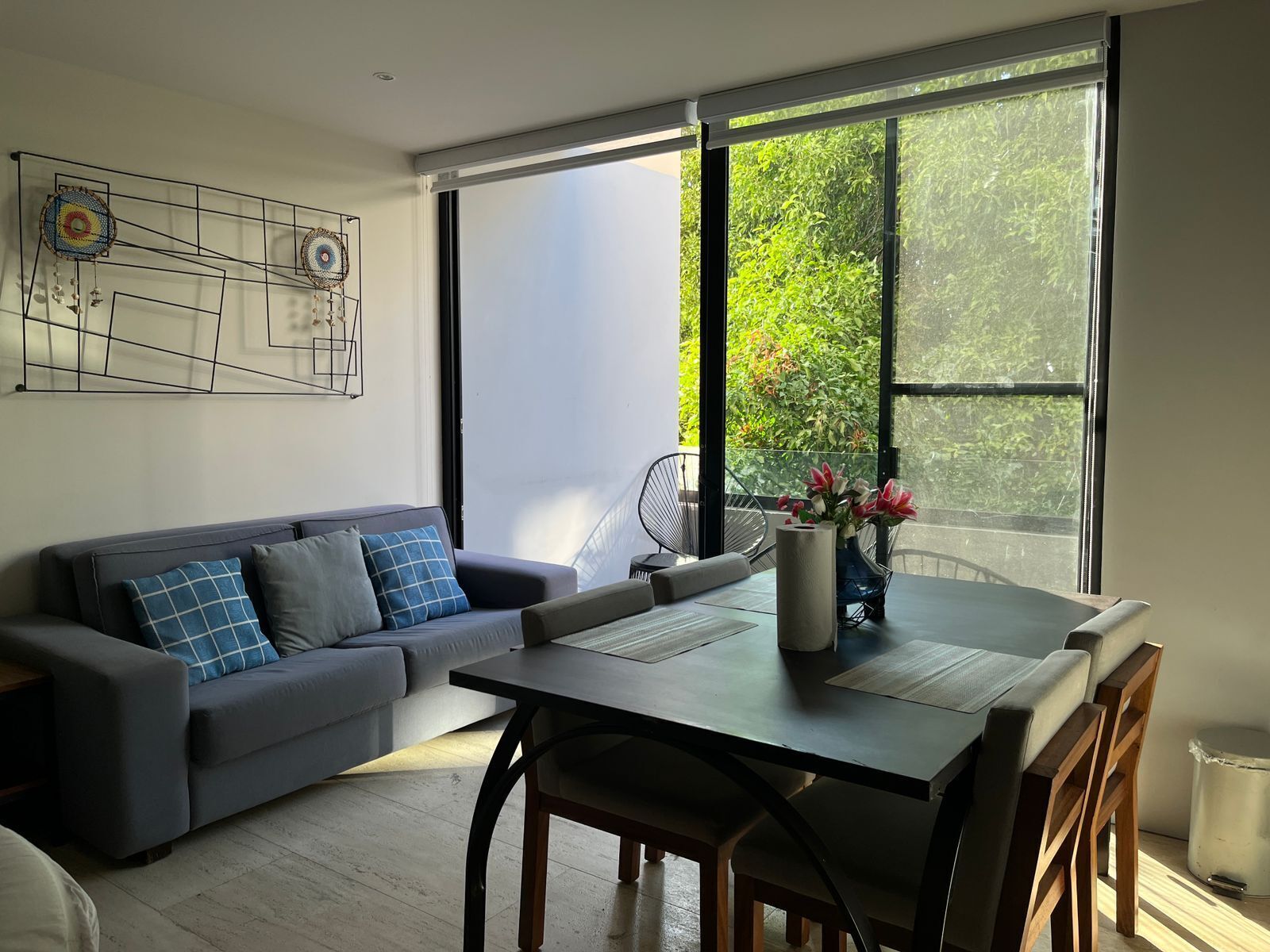Un salon moderne comprenant un canapé, une table à manger, des chaises et une grande fenêtre donnant sur un paysage verdoyant.