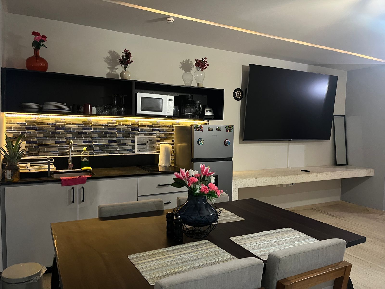 A modern kitchen with a microwave, refrigerator, and a flat-screen TV mounted on the wall.