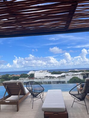 Un espace aménagé au bord de la piscine, avec des chaises longues et une vue sur l’océan et les bâtiments.