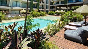 A pool area with lounge chairs, a palm tree, and a modern building with balconies. - Deluxe studio in downtown Tulum with pool, rooftop and gymnasium (Tulum)