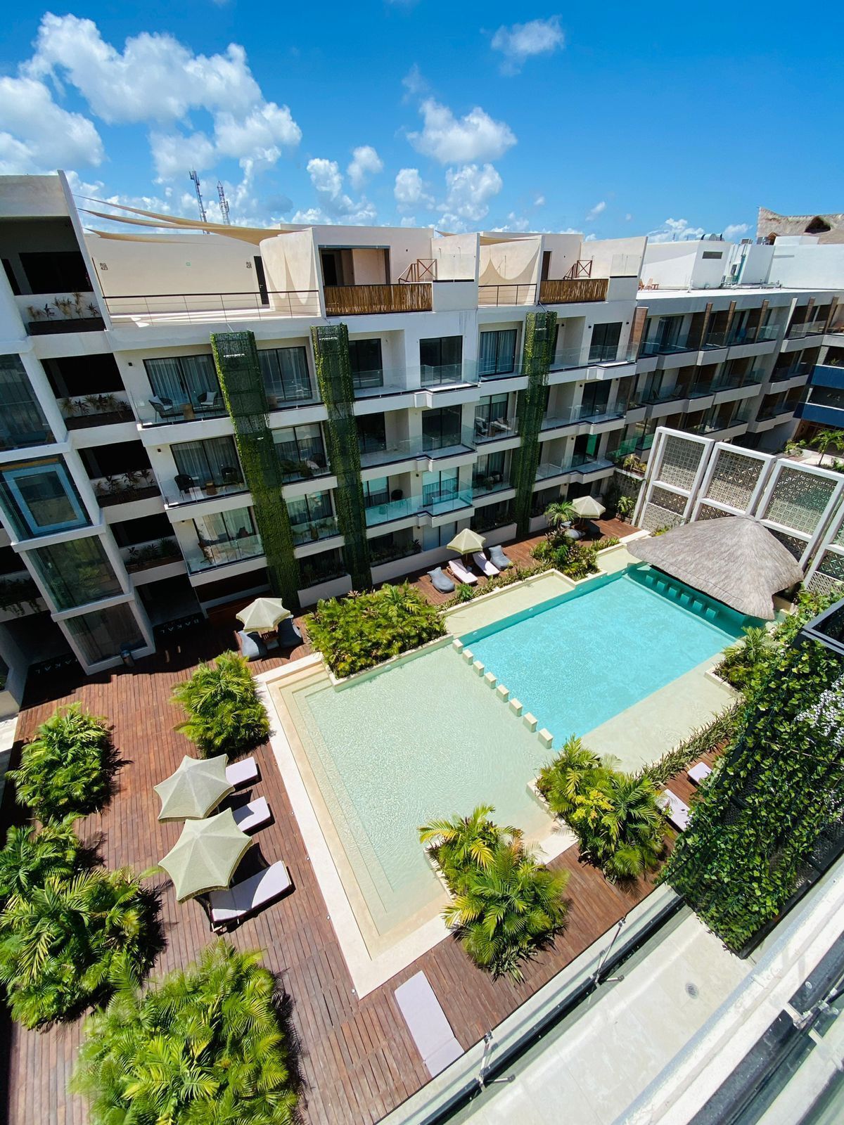 A multi-story hotel with a rooftop pool, outdoor seating, and lush greenery.
