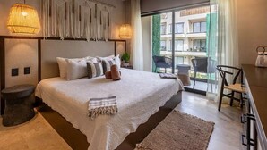 A bedroom with a large bed, a nightstand, a chair, a desk, and a balcony with a view of buildings. - Deluxe studio in downtown Tulum with pool, rooftop and gymnasium (Tulum)