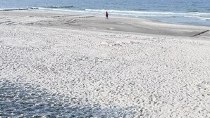 Una amplia playa de arena con una persona de pie a lo lejos.