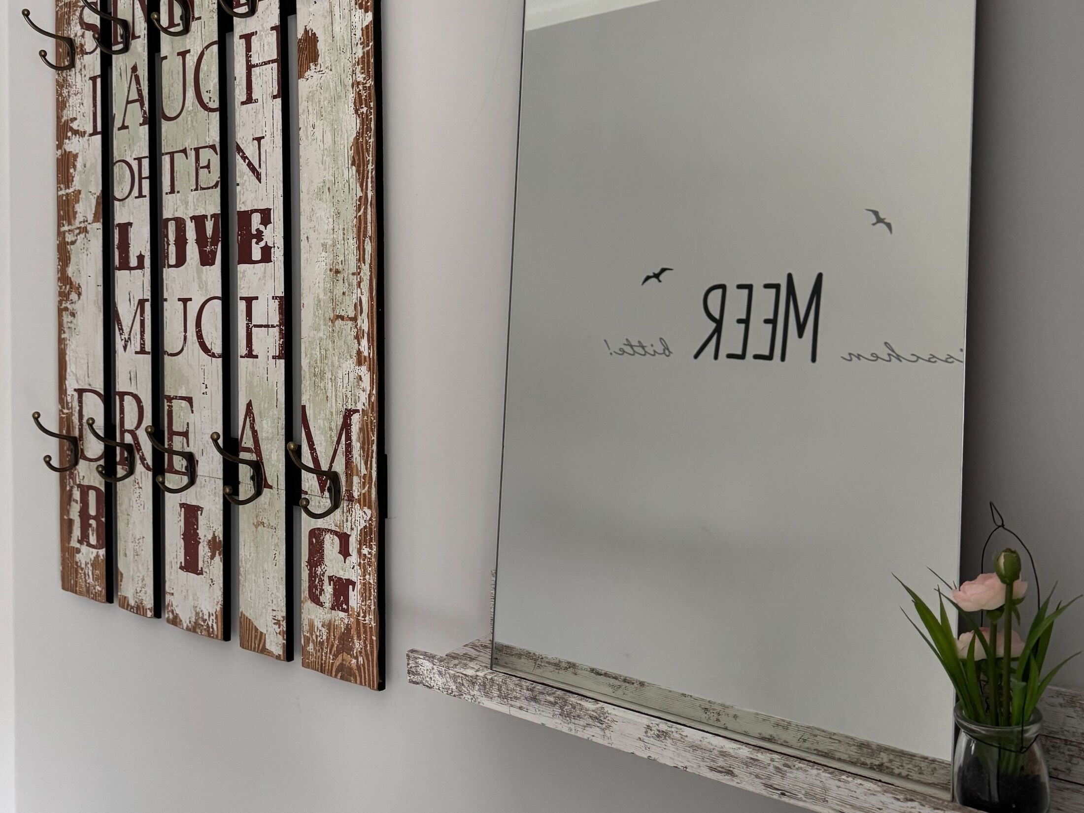A wall with a decorative sign featuring motivational phrases and a small vase with flowers.
