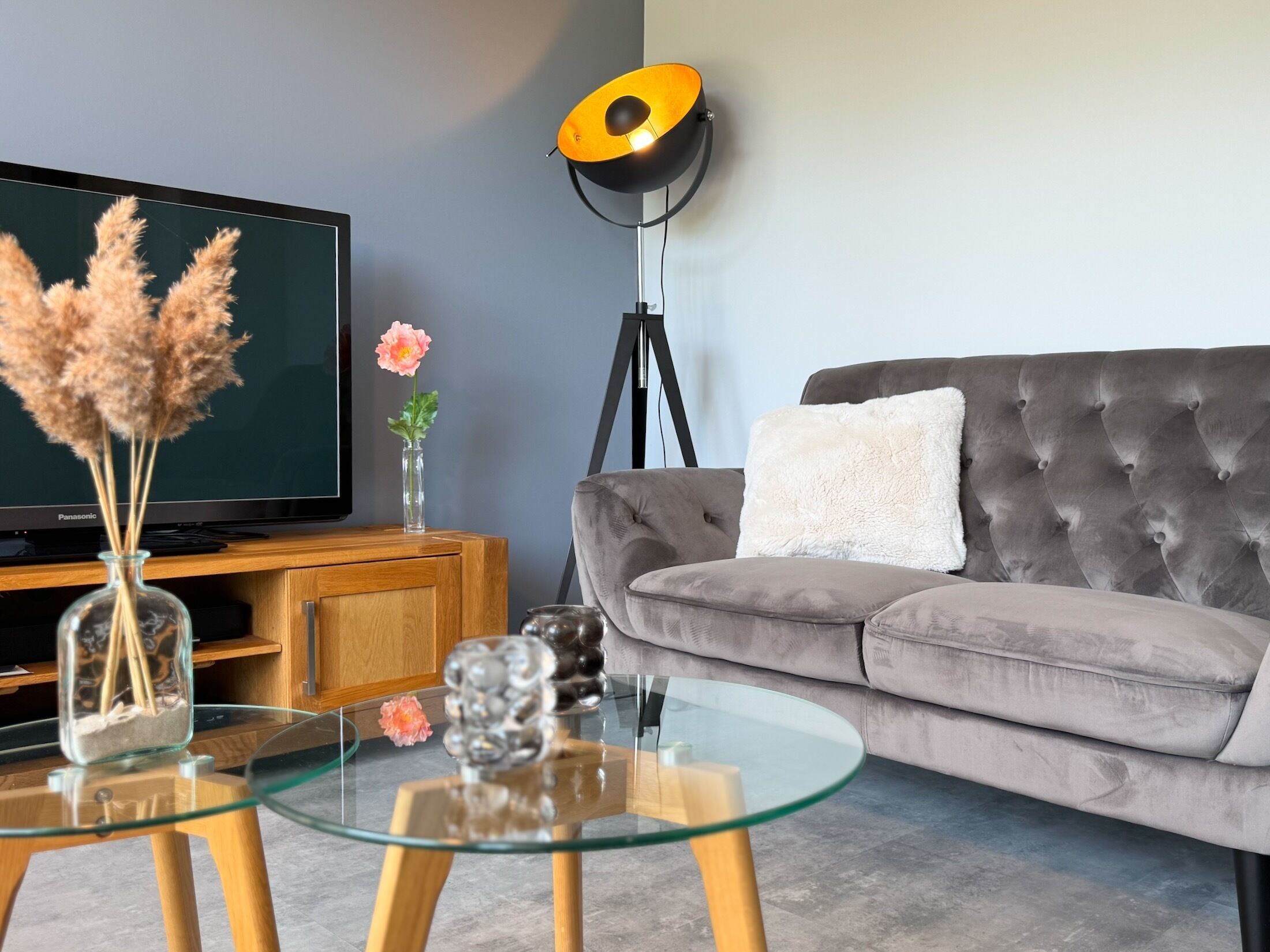 A living room with a television, sofa, glass coffee table, and decorative items.
