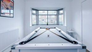 Ein Billardtisch in einem Raum mit einem großen Fenster, einer Heizung und einem gerahmten Kunstwerk an der Wand.