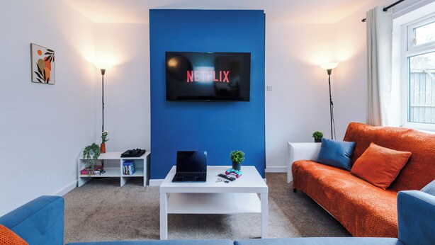 Ein modernes Wohnzimmer mit blauer Akzentwand, einem Flachbildfernseher, einem weißen Couchtisch und einem blauen Sofa.