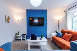 En moderne stue med en blå accentvæg, et fladskærms-tv, et hvidt sofabord og en blå sofa.