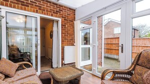 A room with wicker furniture, a sliding glass door, and a brick wall. - Snug 3BR House | Contractors | Parking | Pool Table (Rolleston-on-Dove)