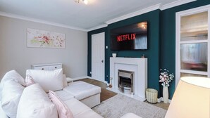 A living room with a white sofa, a fireplace, a TV mounted above it, and a door to the left. - Snug 3BR House | Contractors | Parking | Pool Table (Rolleston-on-Dove)